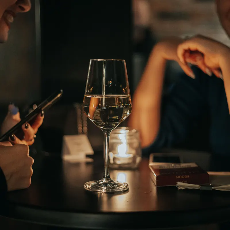 Zwei Freundinnen unterhalten sich abends an einem Bartisch, ein Glas Wein zwischen ihnen